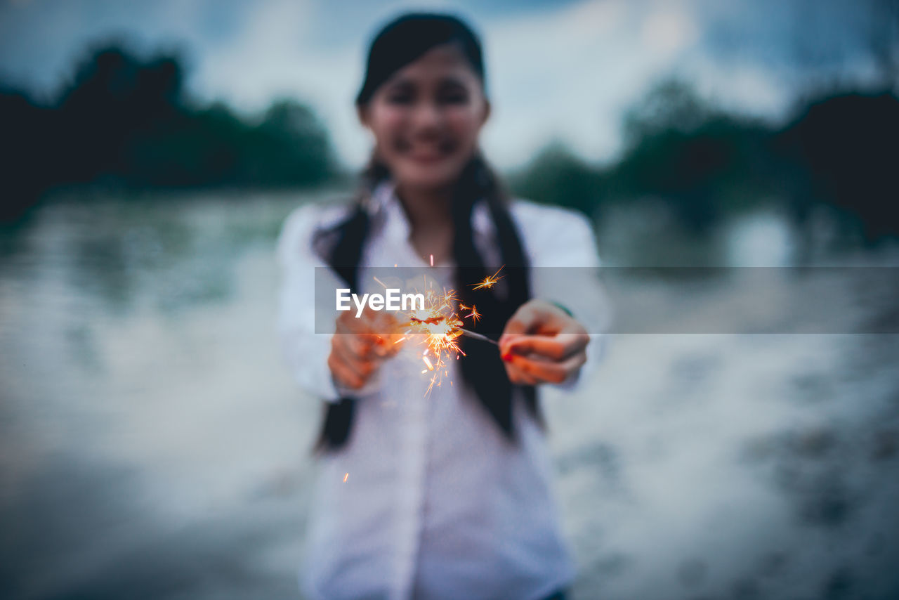 Smiling woman holding sparkler while standing outdoors