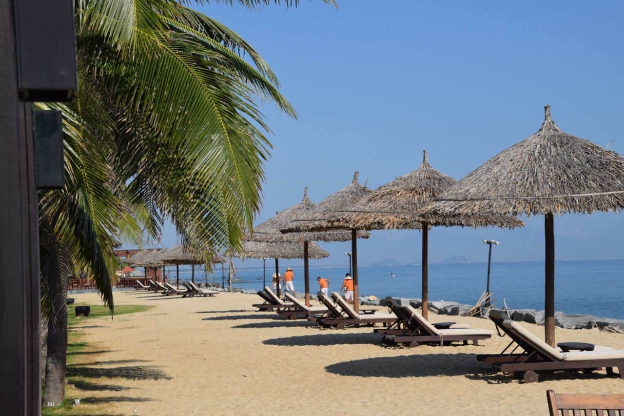 Thatched roof umbrellas and lounge chairs at beach against sky