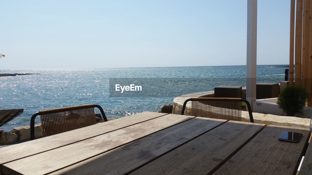 Empty chairs by swimming pool against sea against clear sky