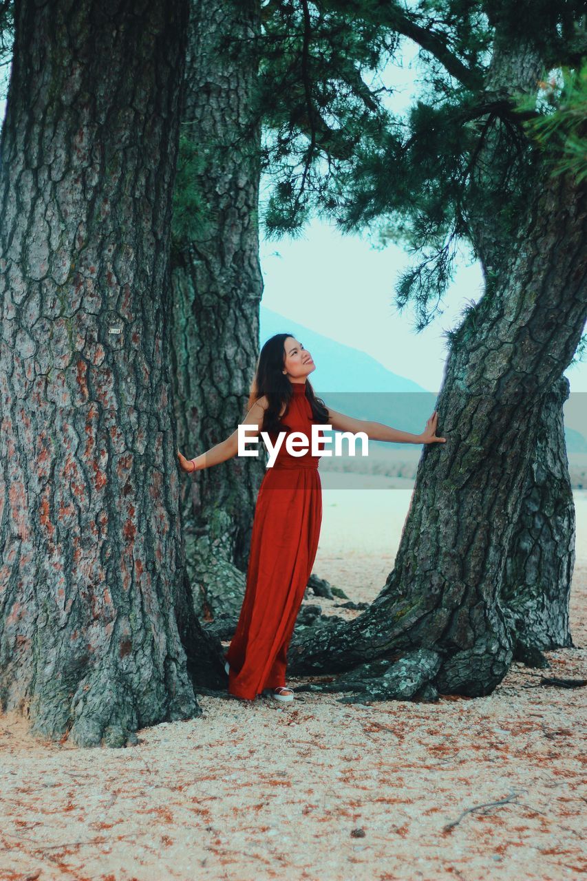 Young woman standing by tree trunk