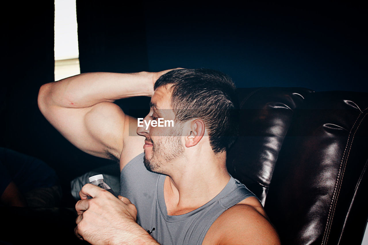 Young man showing biceps while sitting on sofa at home