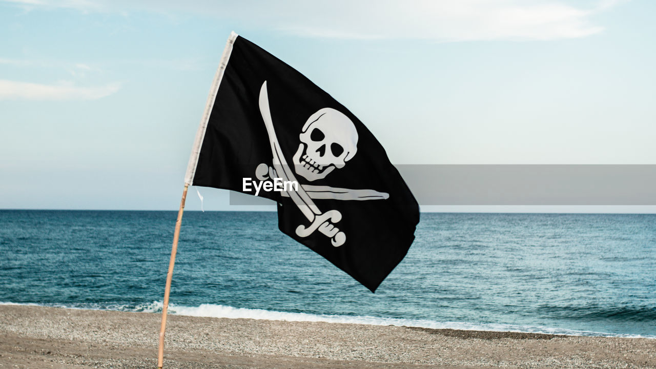 Black pirate flag with skull symbol on the desert island