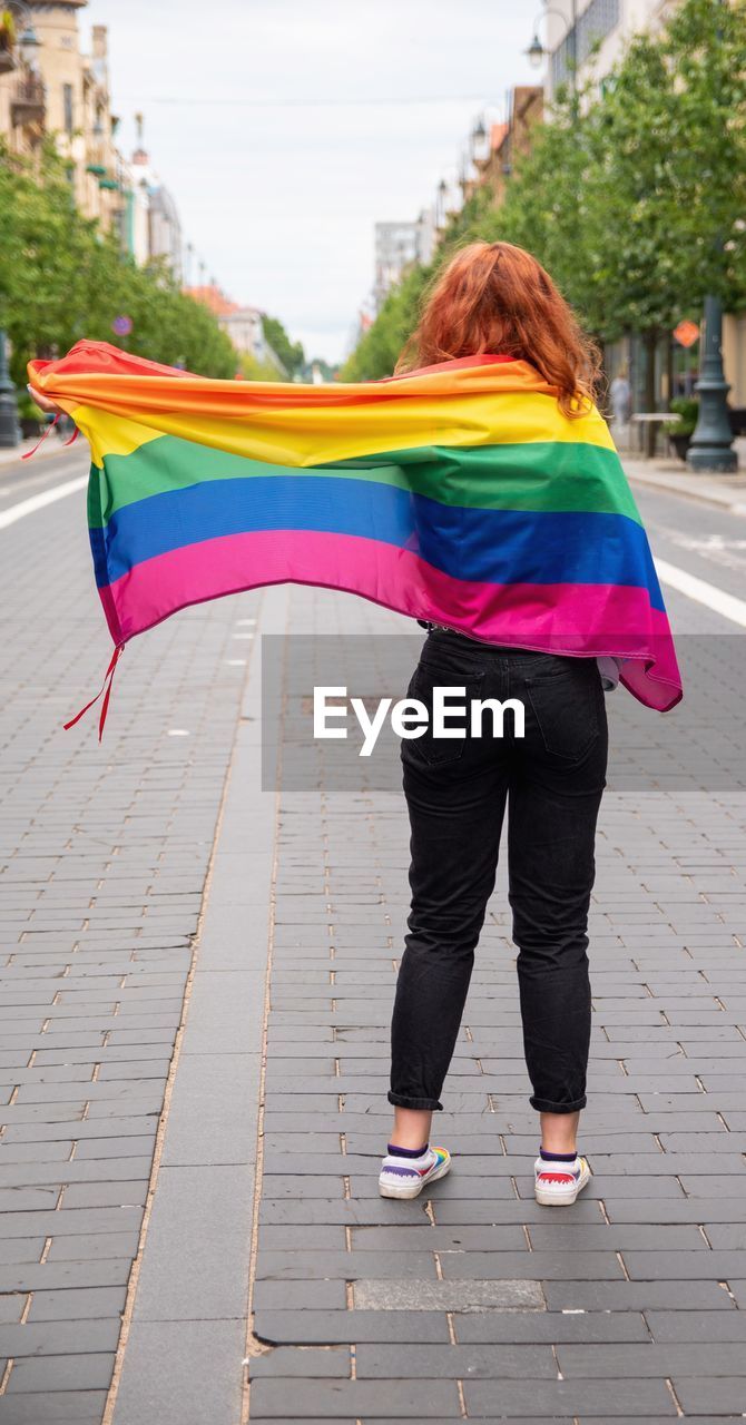 Rear view of girl with rainbow flag on road