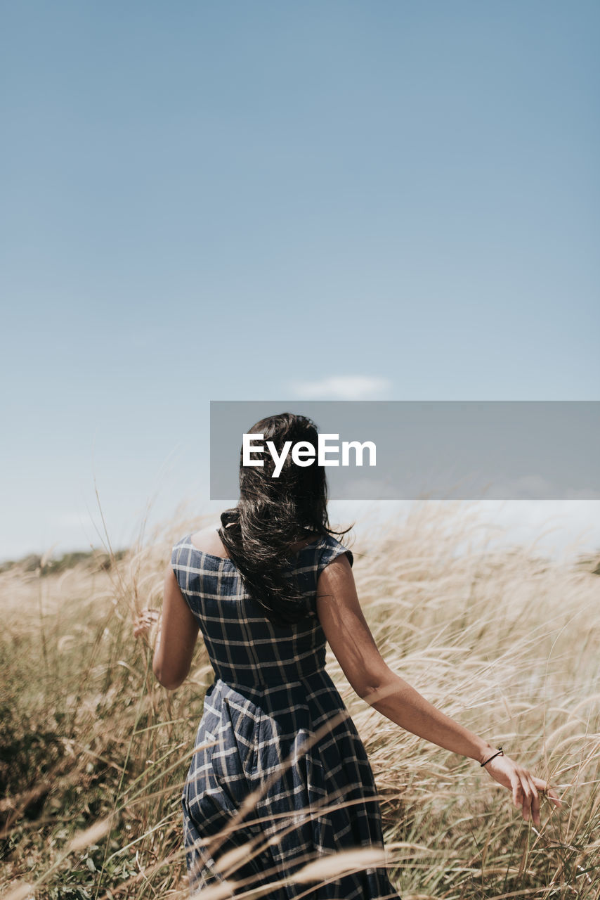 Rear view of woman walking on grassy field against sky