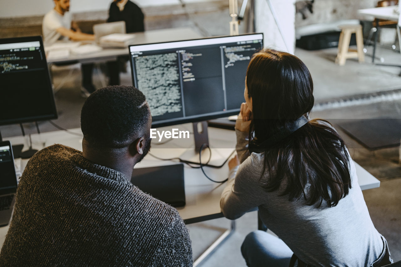 Male and female programmers coding over computer in creative office