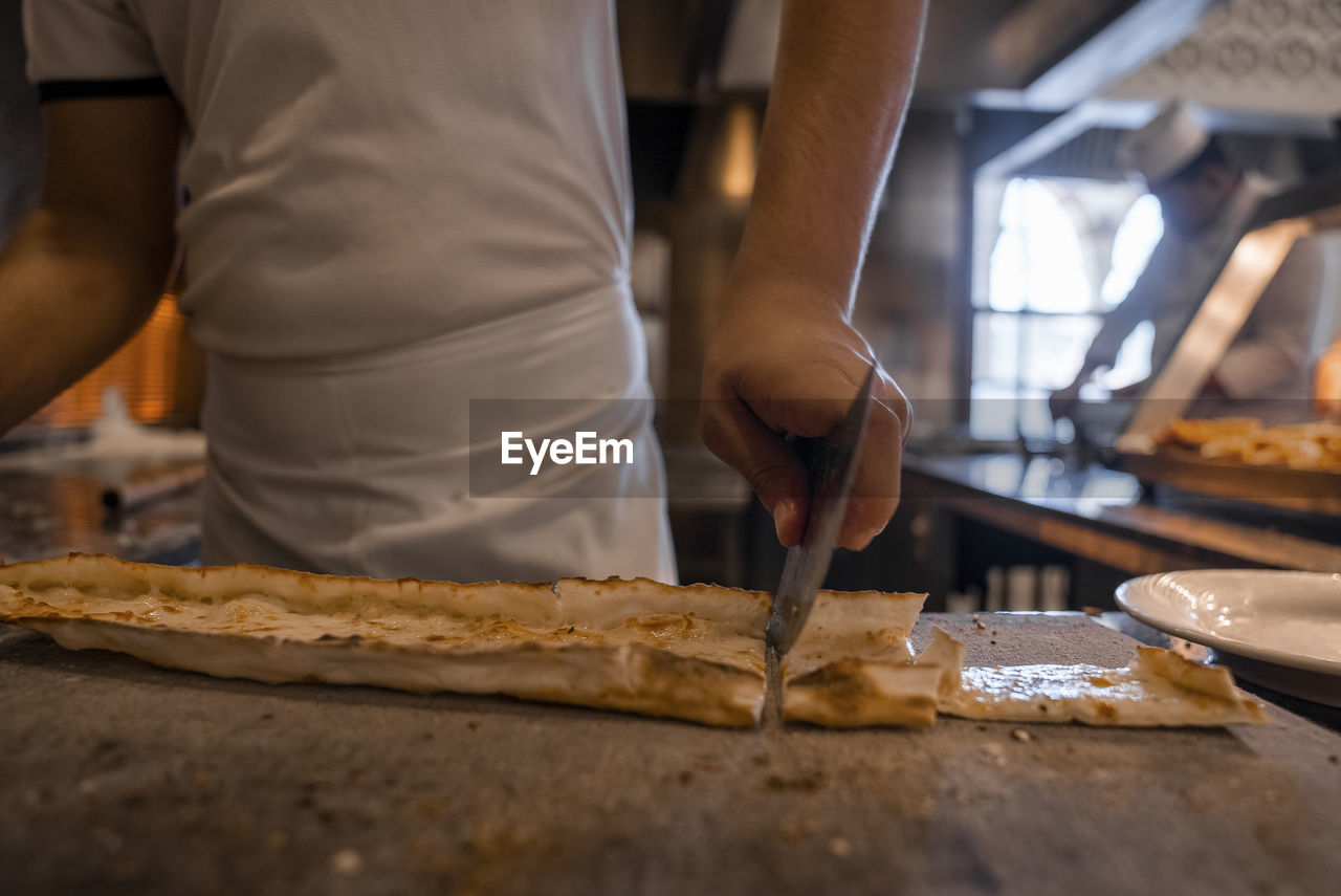 Chef cutting turkish cheese pide into slices on table at restaurant