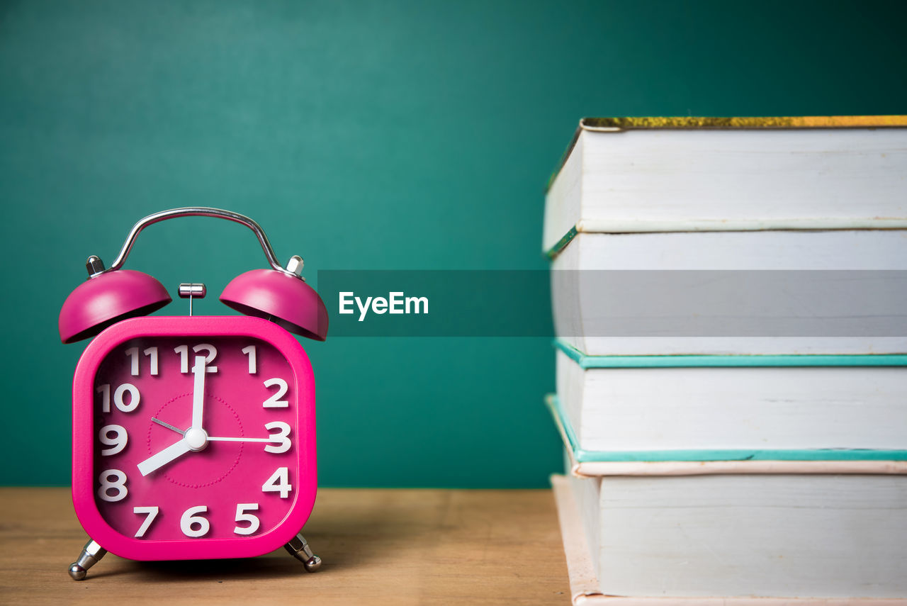 Close-up of alarm clock and books on table against green chalkboard