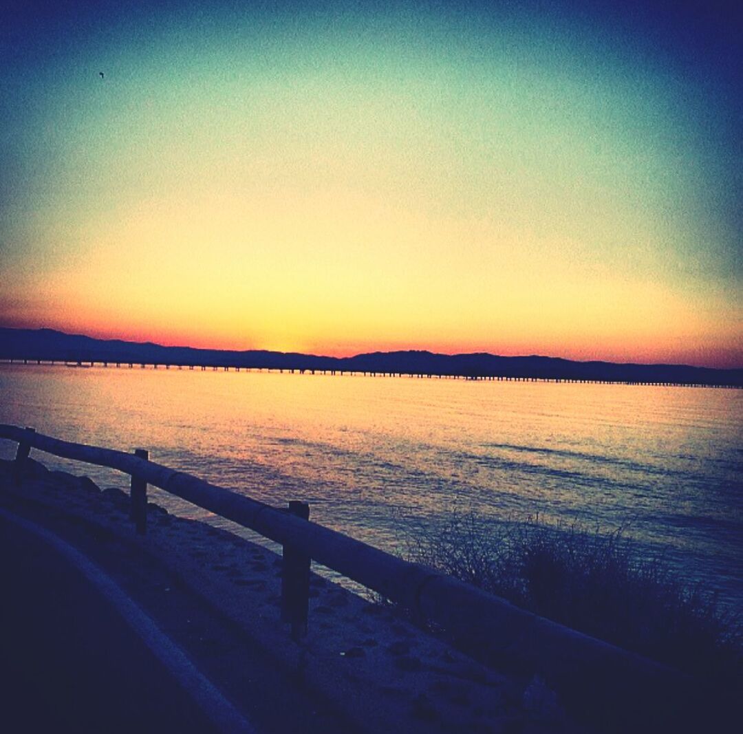 Bridge by sea against clear sky during sunset