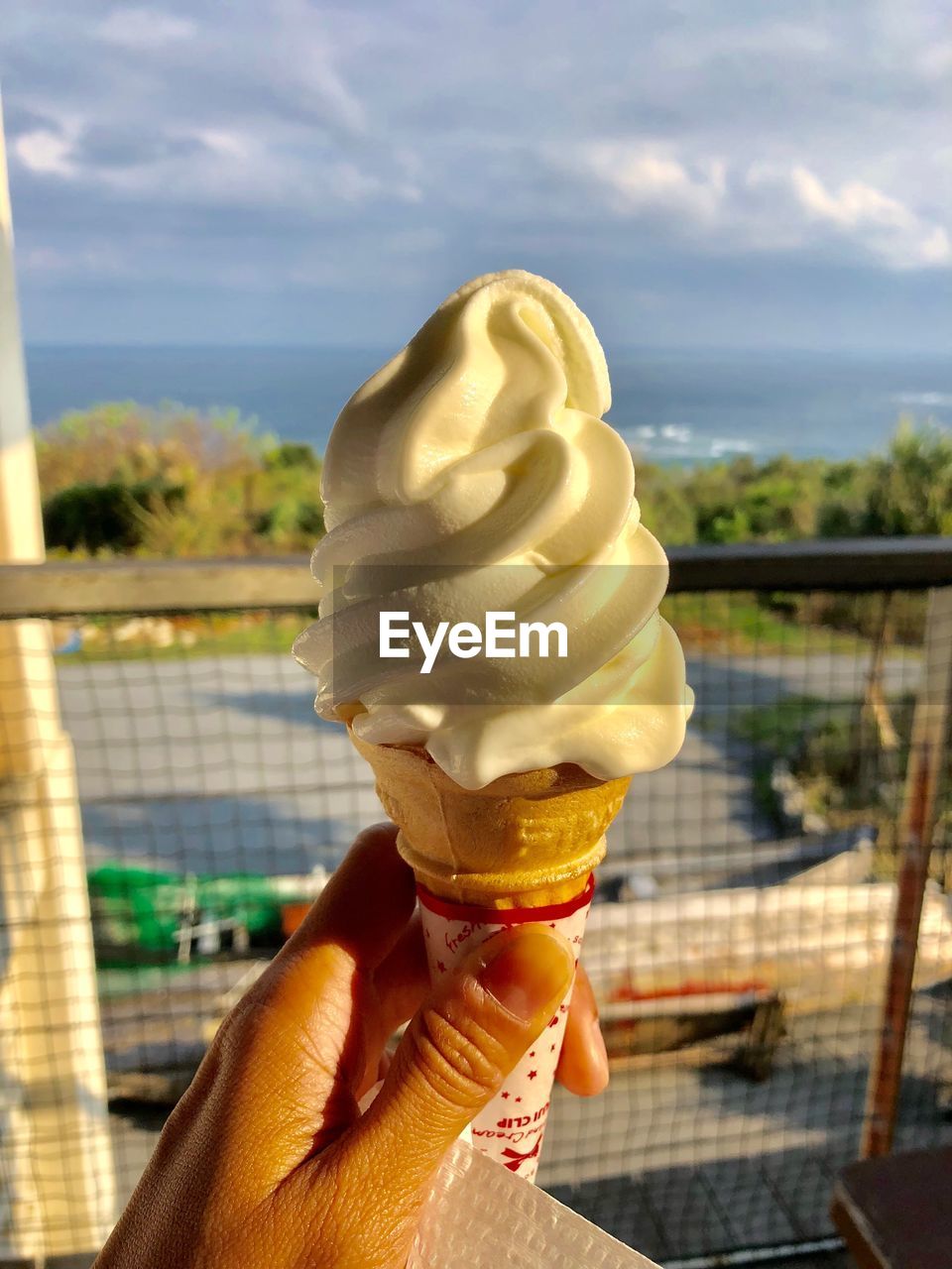 CLOSE-UP OF HAND HOLDING ICE CREAM CONE AGAINST BLURRED BACKGROUND