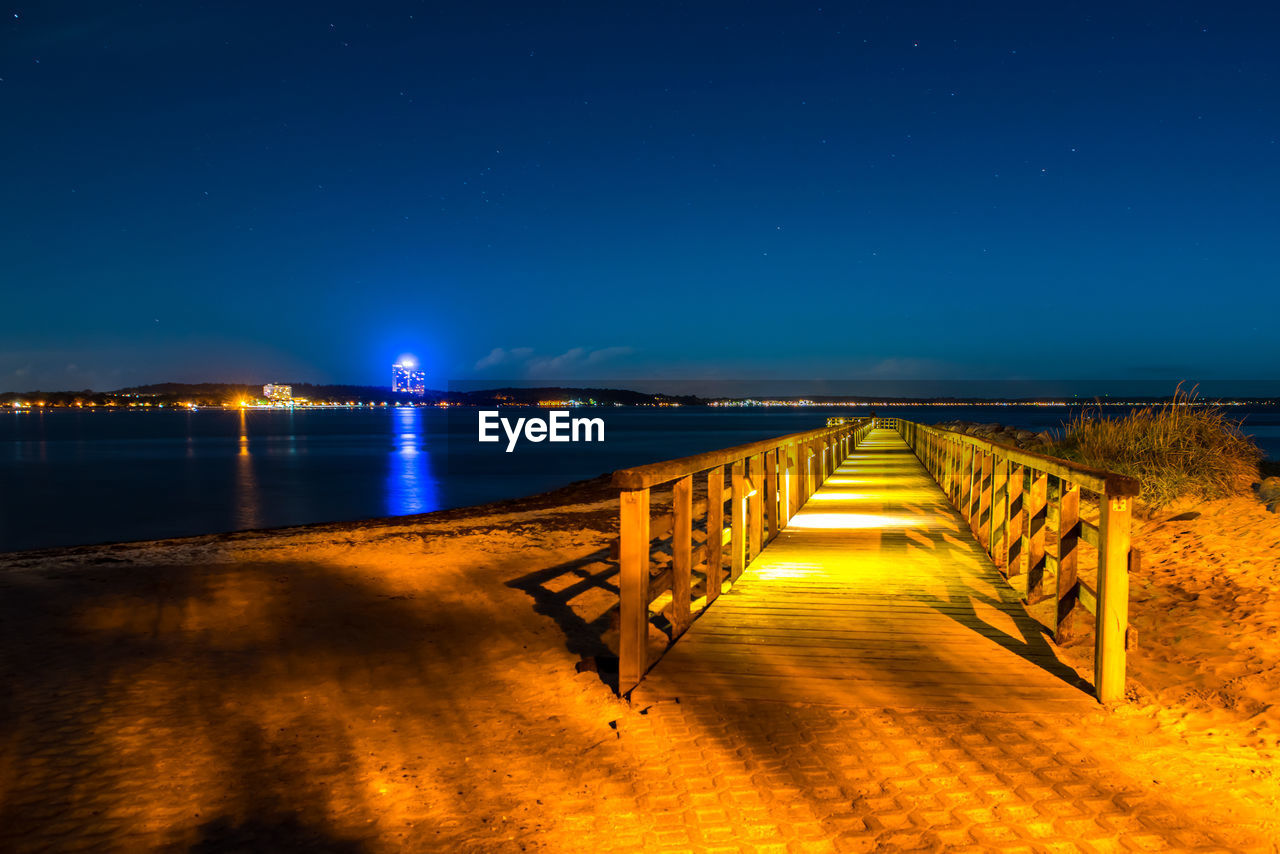 Pier over sea against clear sky at night