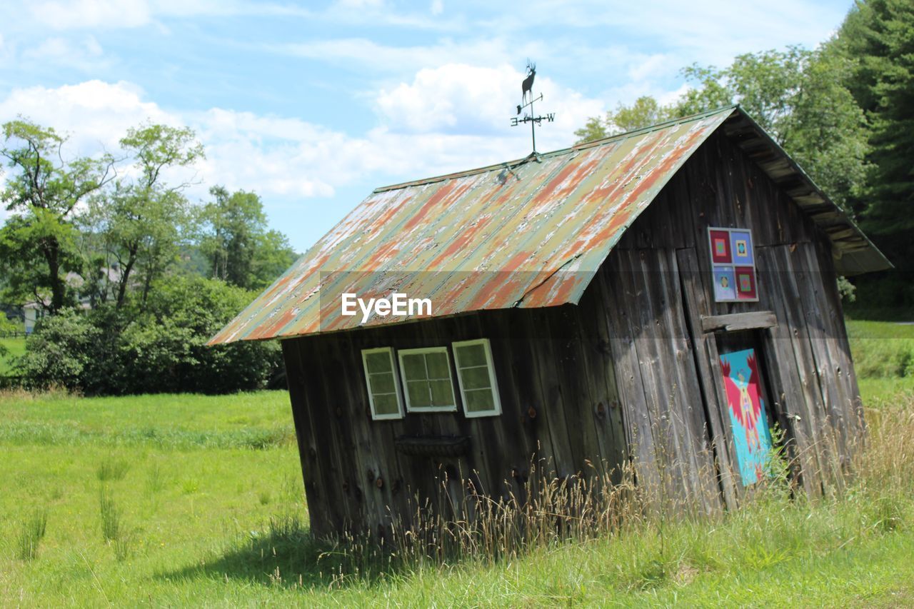 ABANDONED HOUSE ON FIELD AGAINST TREES