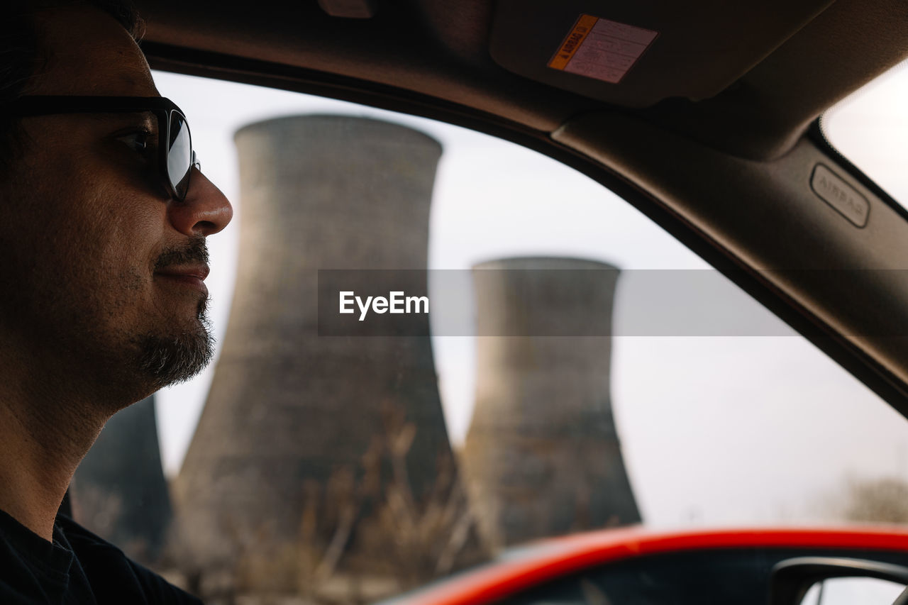 Portrait of man in sunglasses driving car against cooling tower