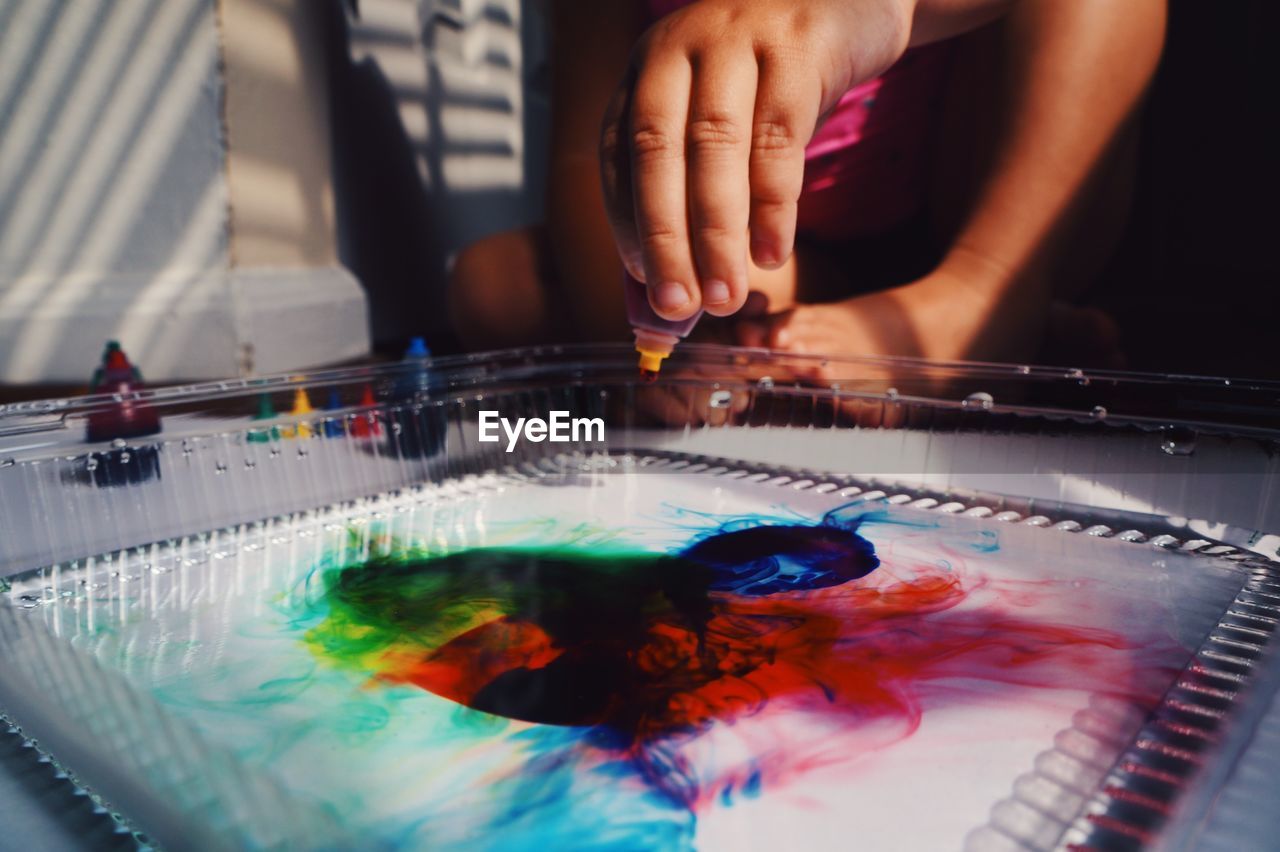 Close-up of girl hand pouring colors in water at home