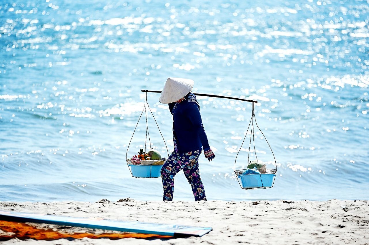 Side view of person carrying baskets against calm blue sea