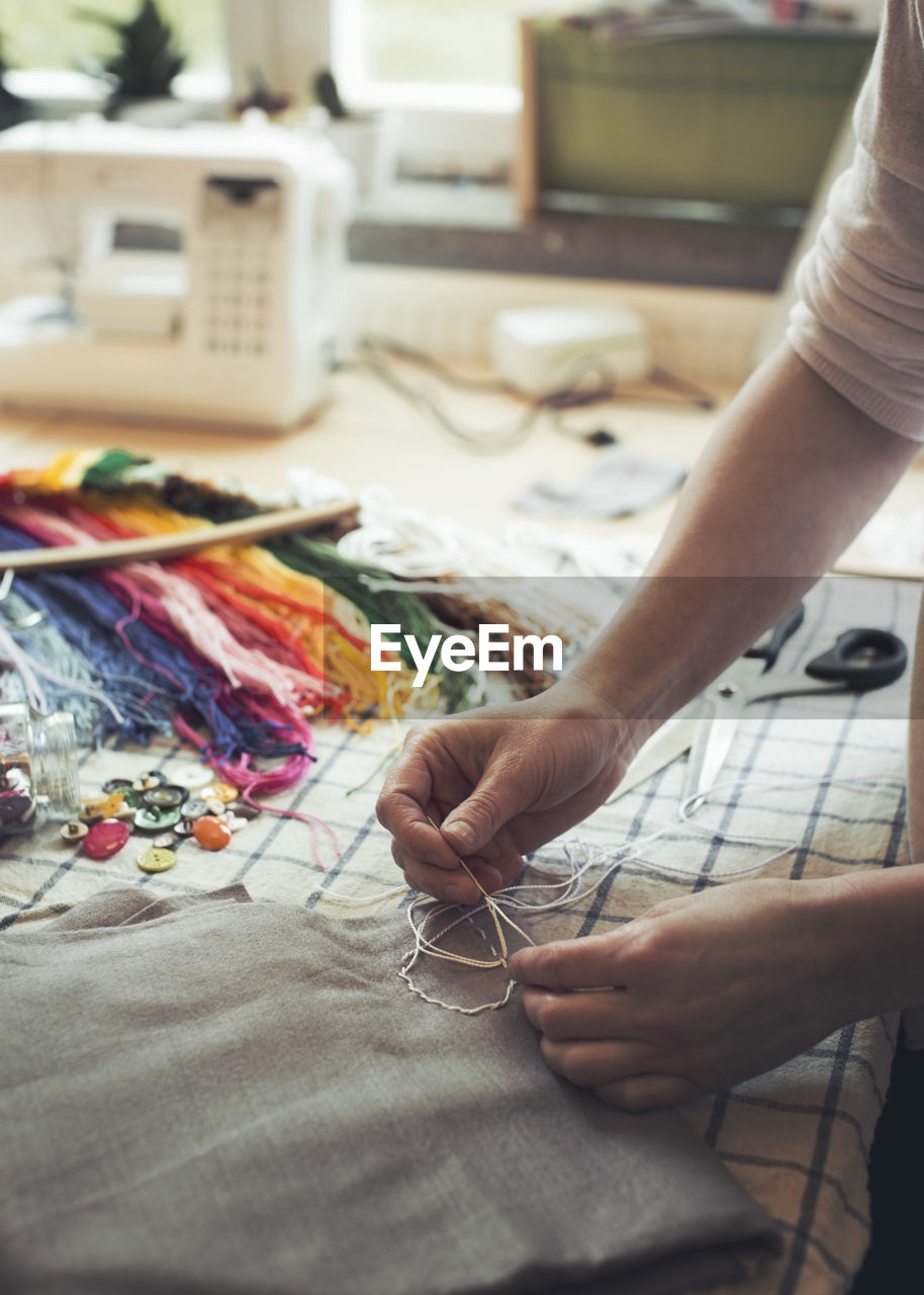 Cropped image of woman stitching fabric on table at home