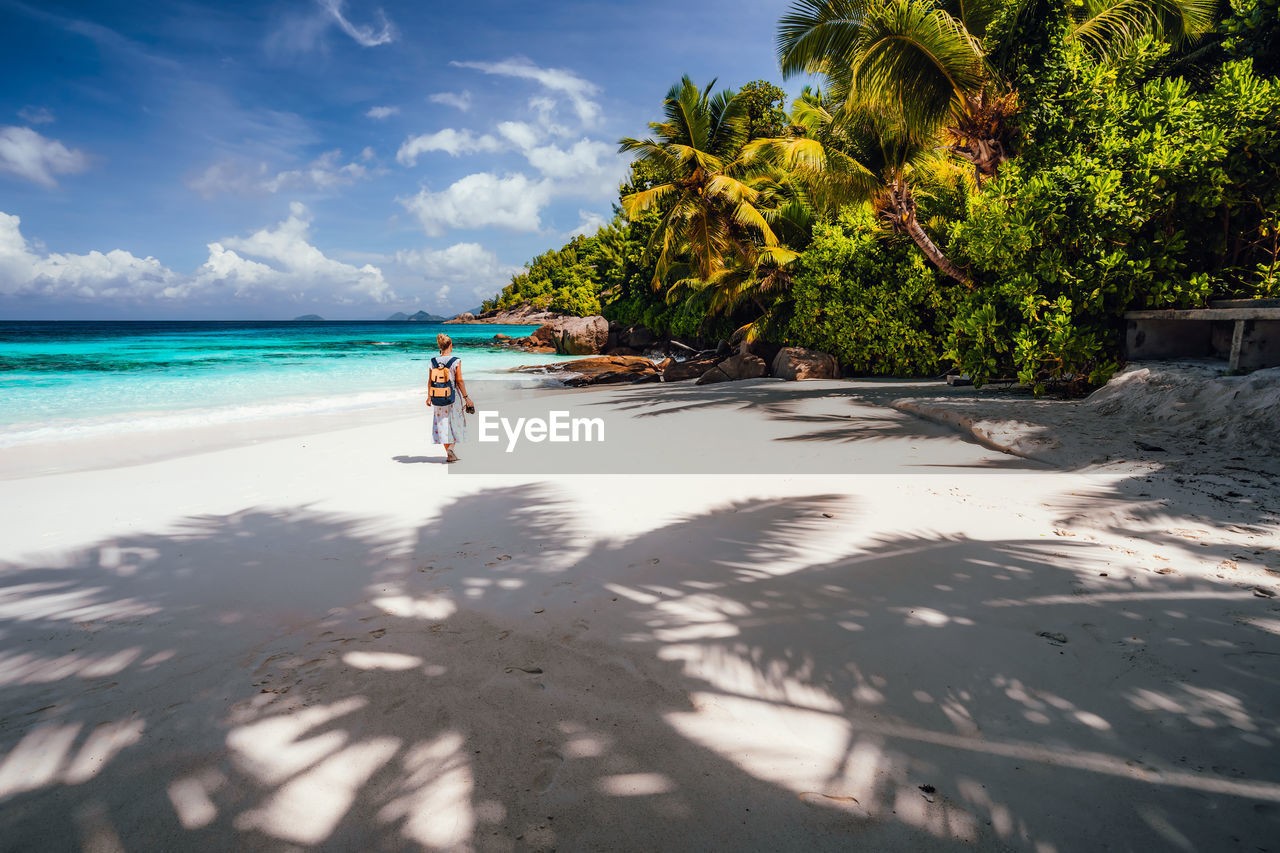 Rear view of woman with backpack walking at beach against sky