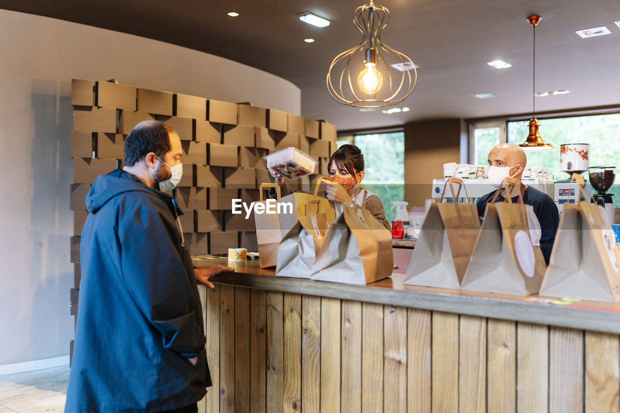 Male and female colleague preparing take out order for customer in restaurant during covid-19