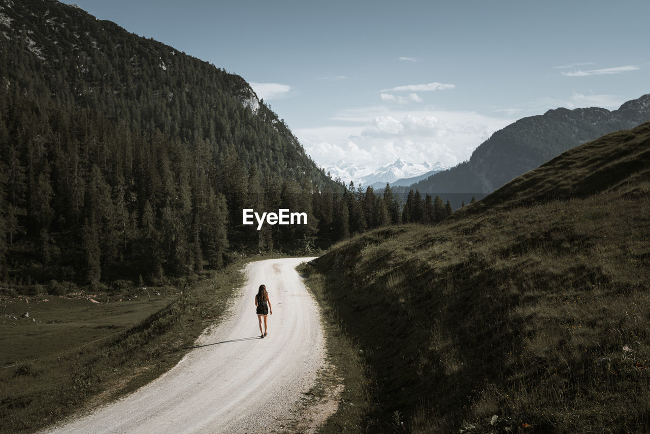 Woman walking on dirt road against sky