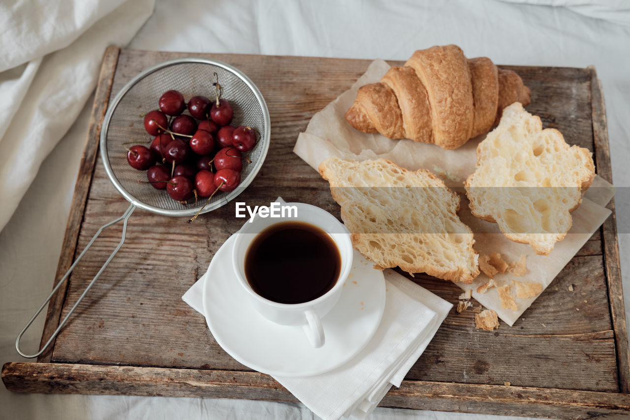 Tasty breakfast with fresh croissant, coffee, cherries on a wooden tray. hearty croissant 