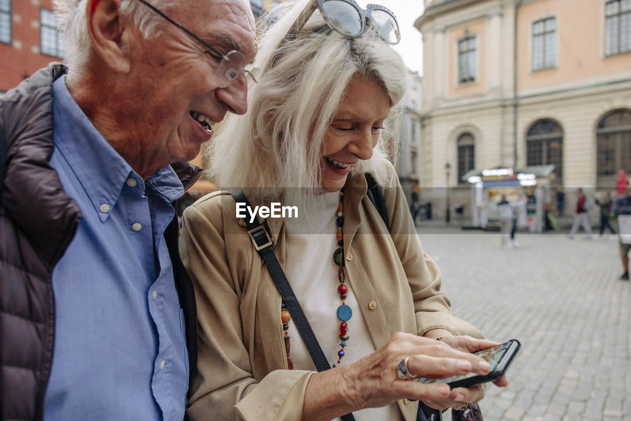 Happy senior couple sharing smart phone while exploring city