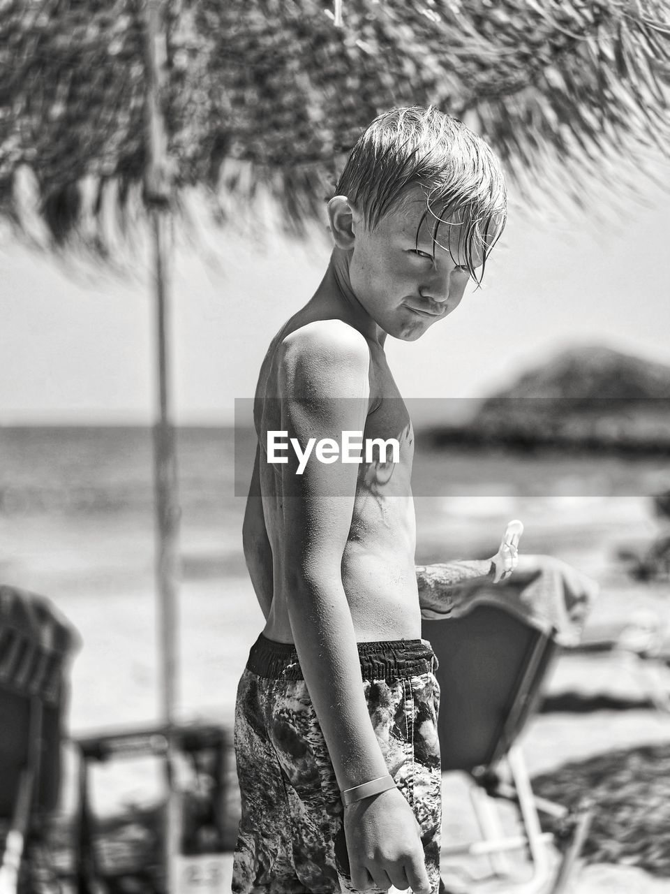 Side view of shirtless boy standing at beach