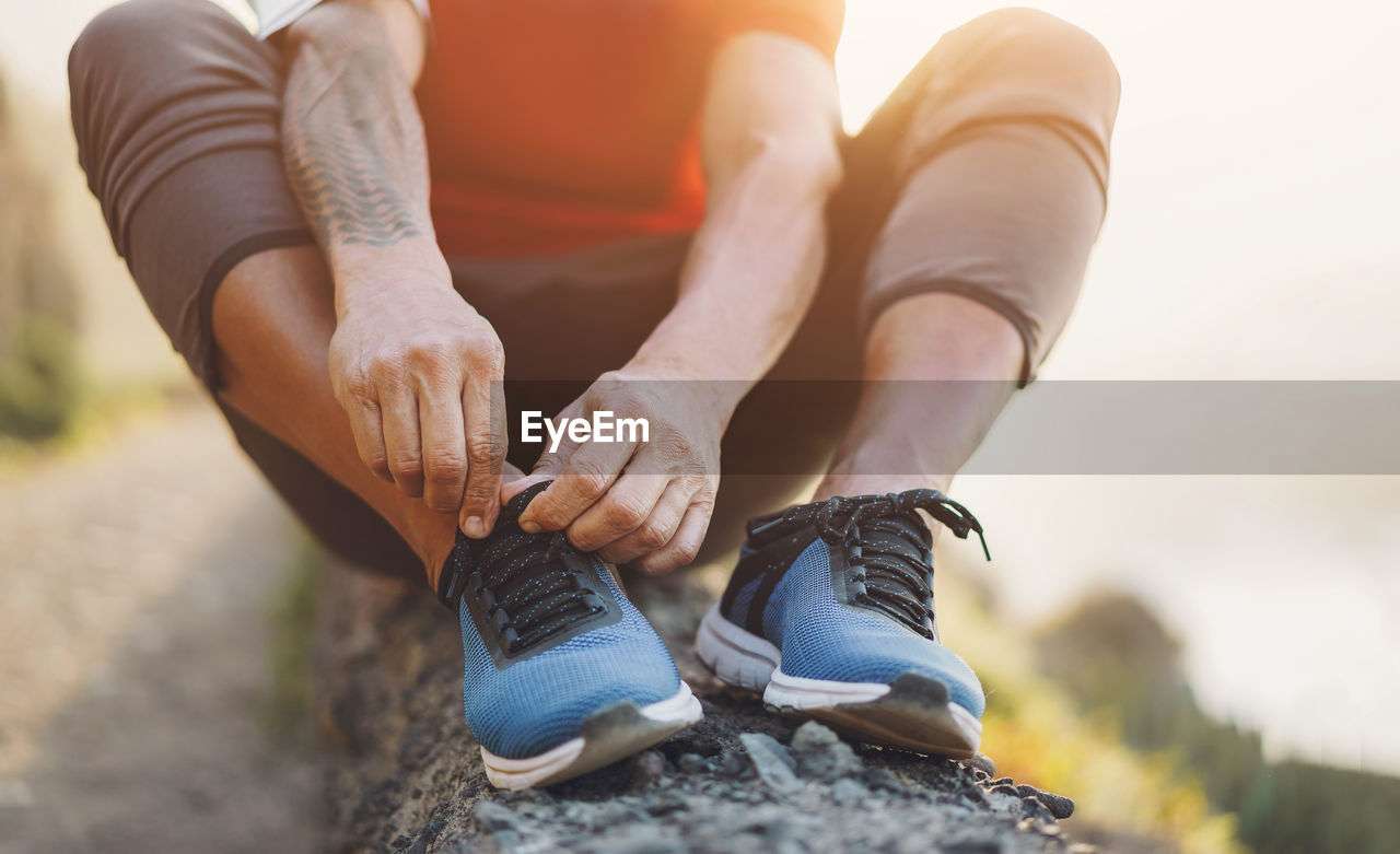 Fit tattoo man tie his sport shoes outdoor during jogging session - focus on hands