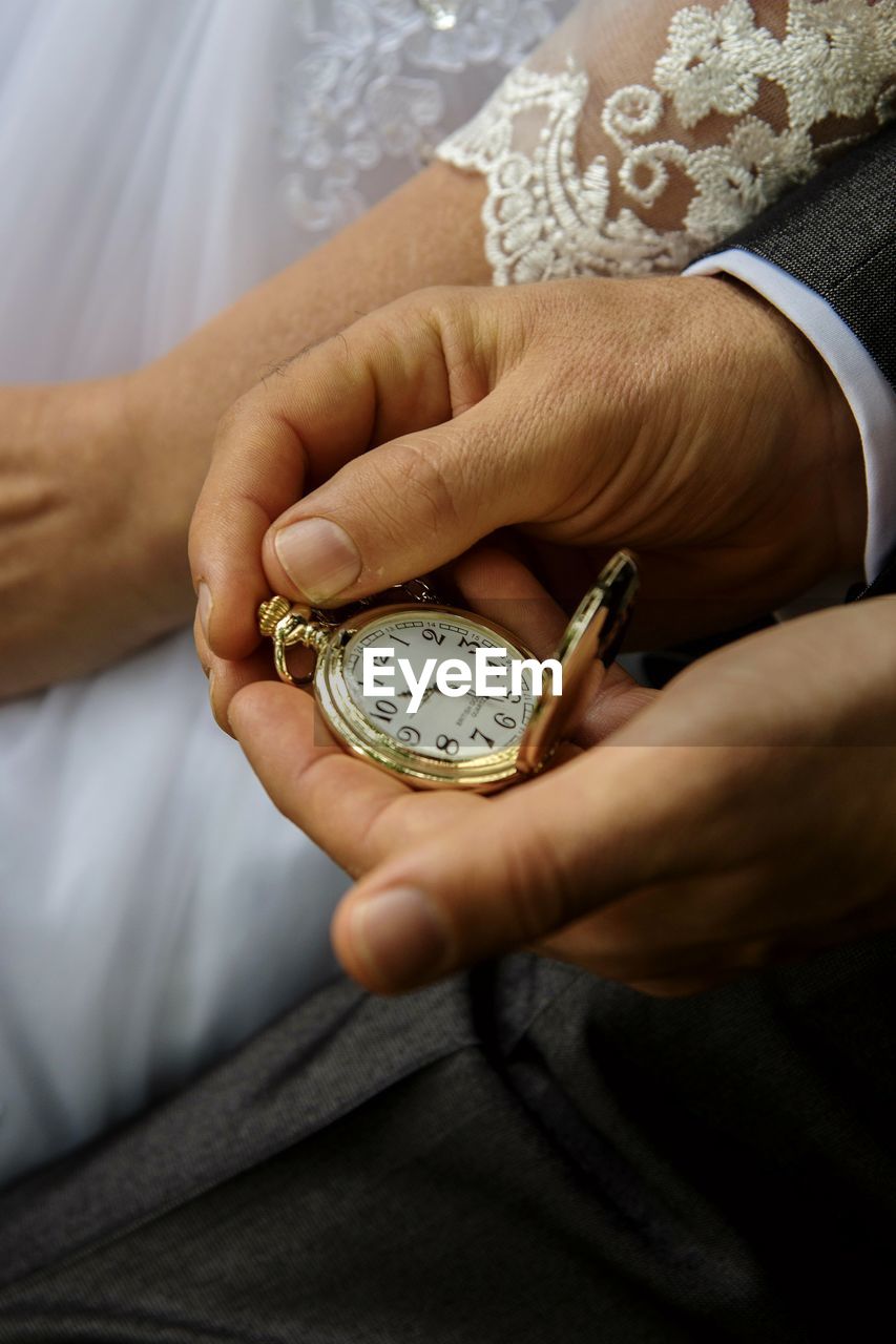 Midsection of groom holding pocket watch by bride