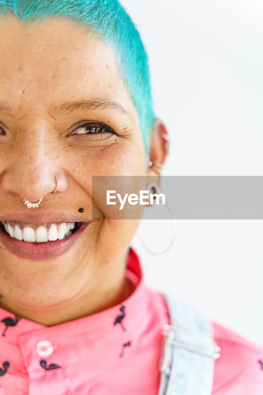 Positive female with colorful dyed short hair in denim wear looking at camera with smile on white background in light room