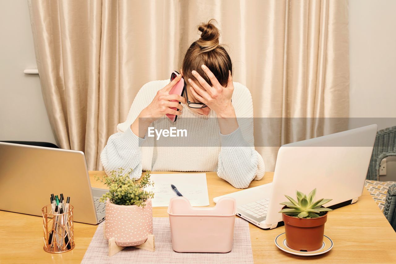 Stressed businesswoman working from her home office using laptop and smartphone