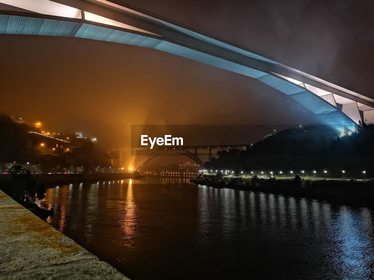 Low angle view of illuminated bridge over river in city at night