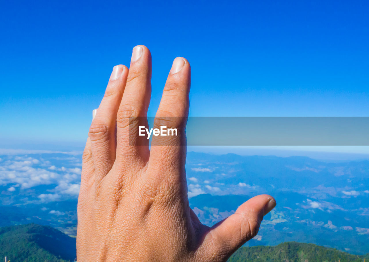 Cropped hand against blue sky