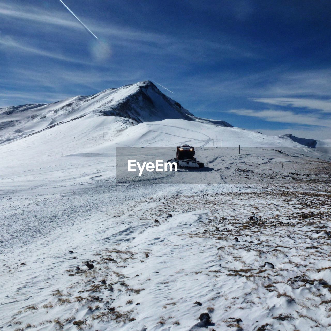 Snow groomer on snowcapped mountain against sky