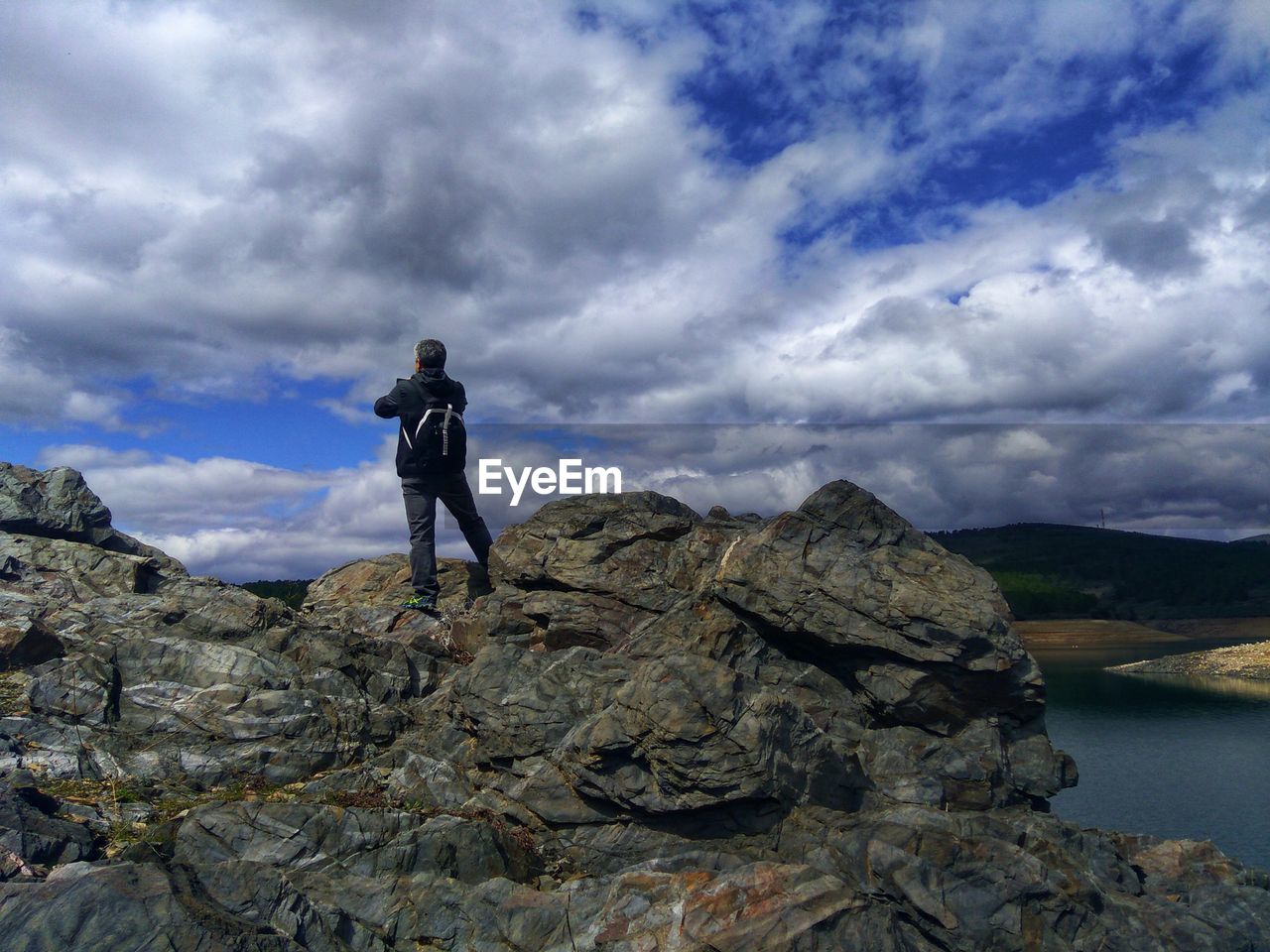 Rear view of man standing on rock and lake against sky