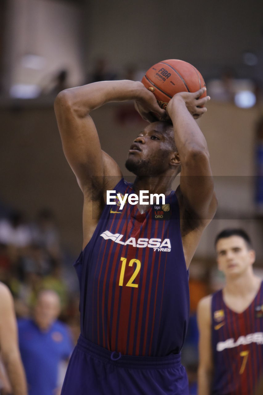 MIDSECTION OF MAN WITH ARMS RAISED STANDING AGAINST BASKETBALL