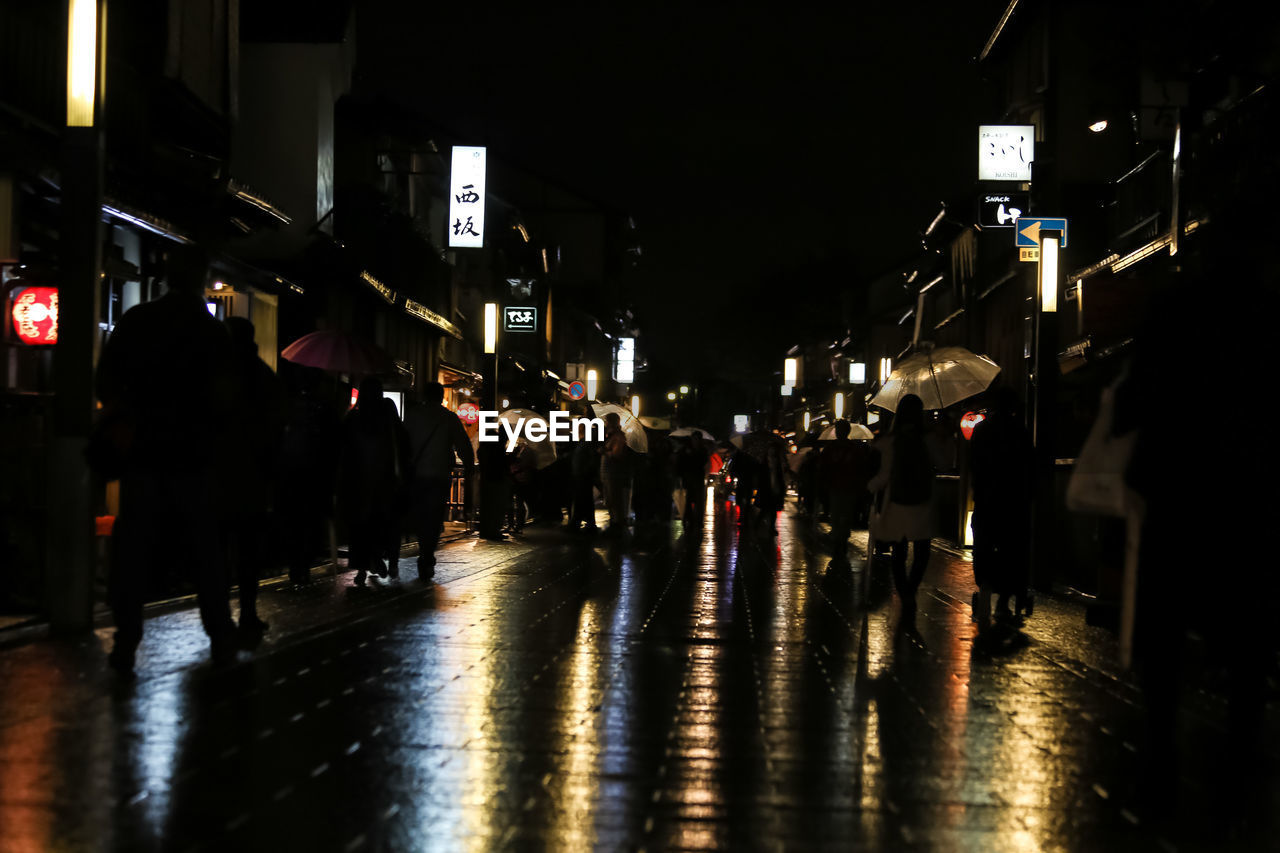 PEOPLE WALKING ON WET STREET IN CITY AT NIGHT