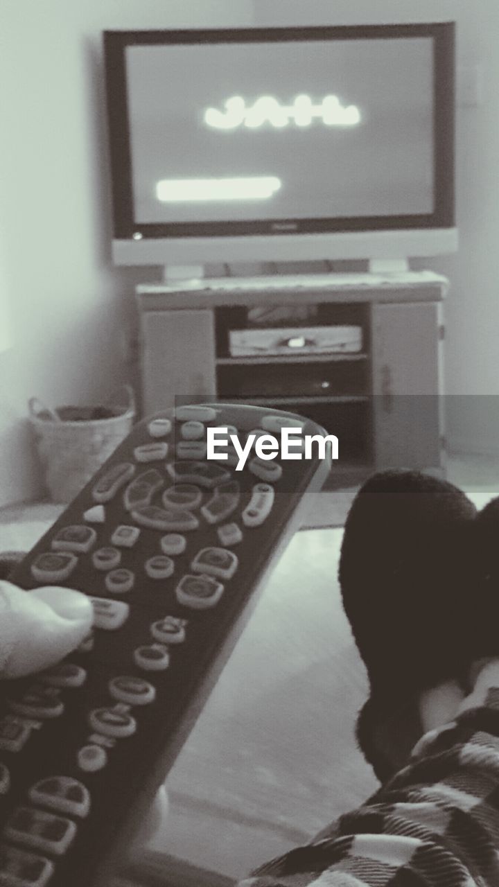 Cropped image of person holding remote control watching television set