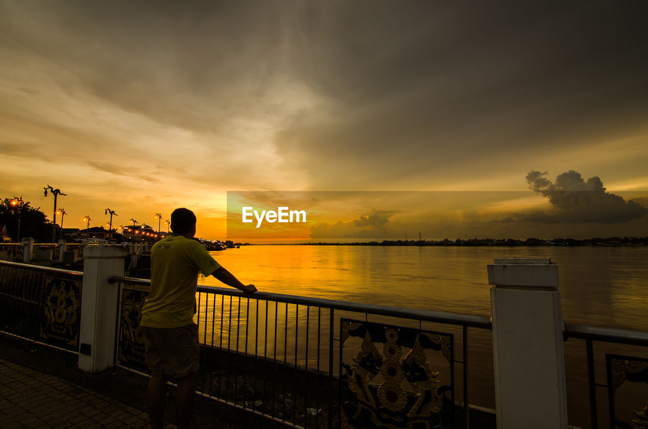 Rear view of man looking at sea against sky during sunset