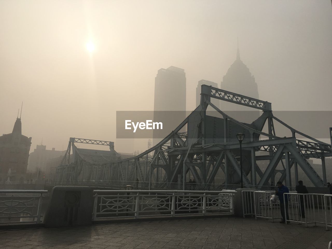 Bridge against buildings during foggy weather on sunny day