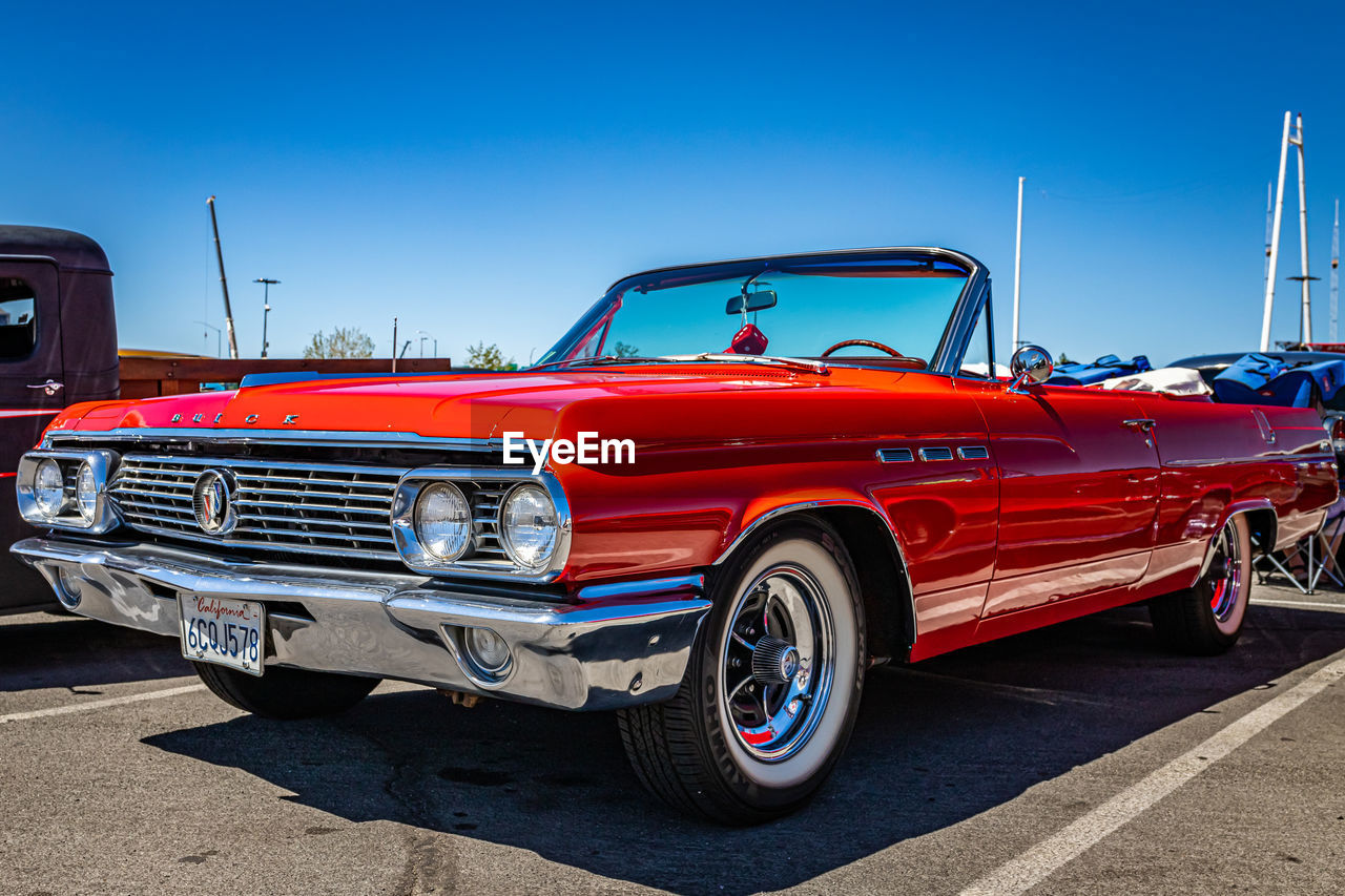 car, vehicle, mode of transportation, transportation, land vehicle, motor vehicle, retro styled, red, automotive exterior, vintage car, blue, sky, collector's car, antique car, road, city, driving, nature, street, convertible, clear sky, architecture