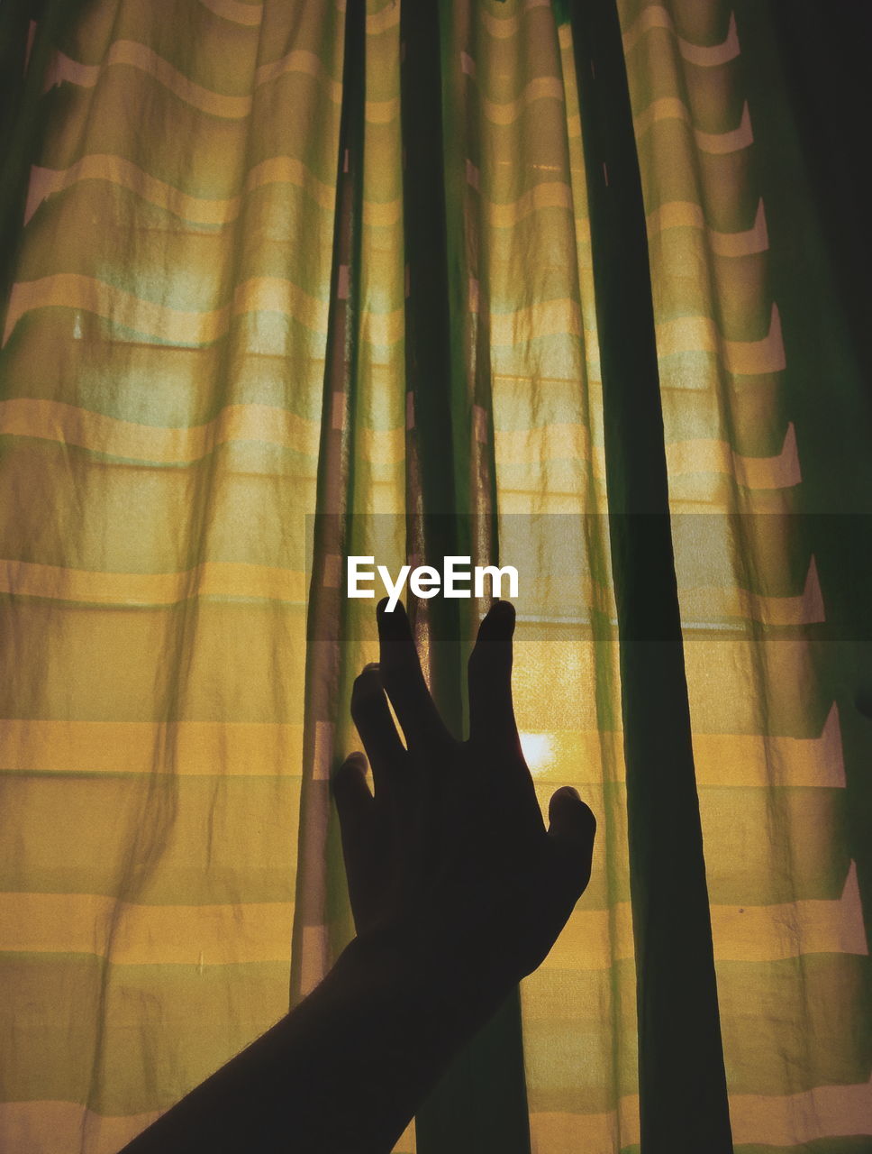 Cropped hand touching curtain at home
