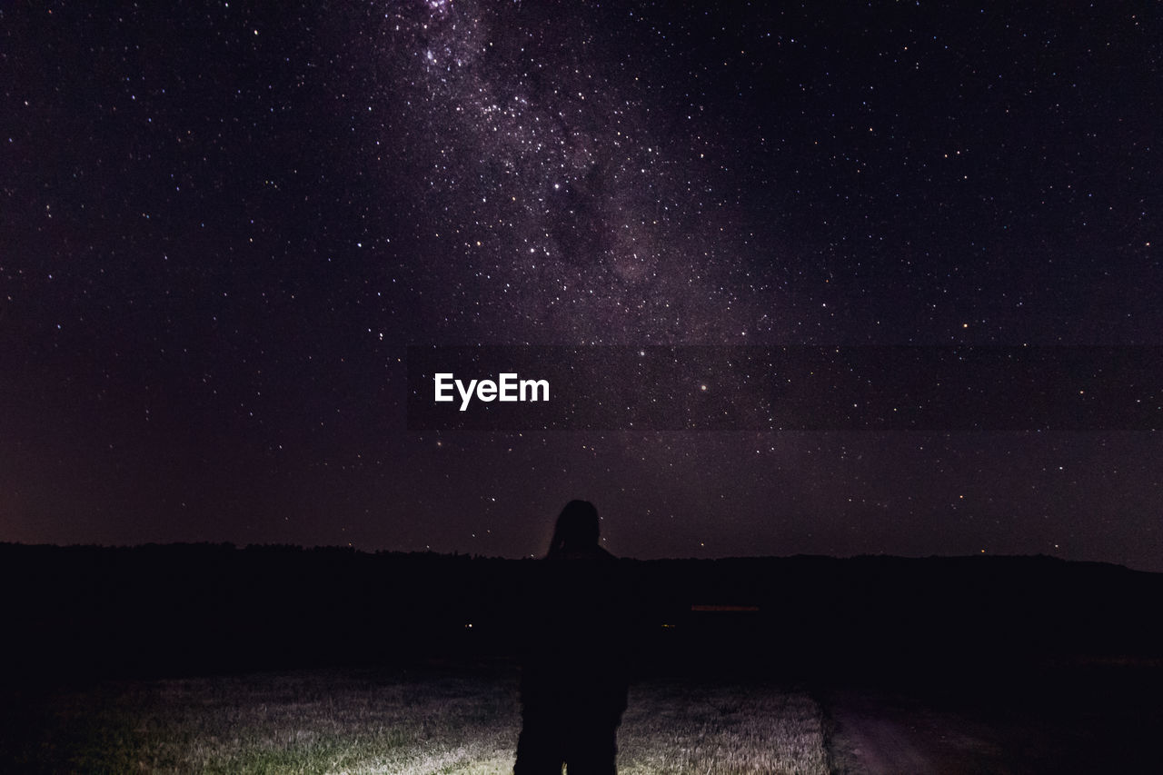 Silhouette man standing against star field in sky at night