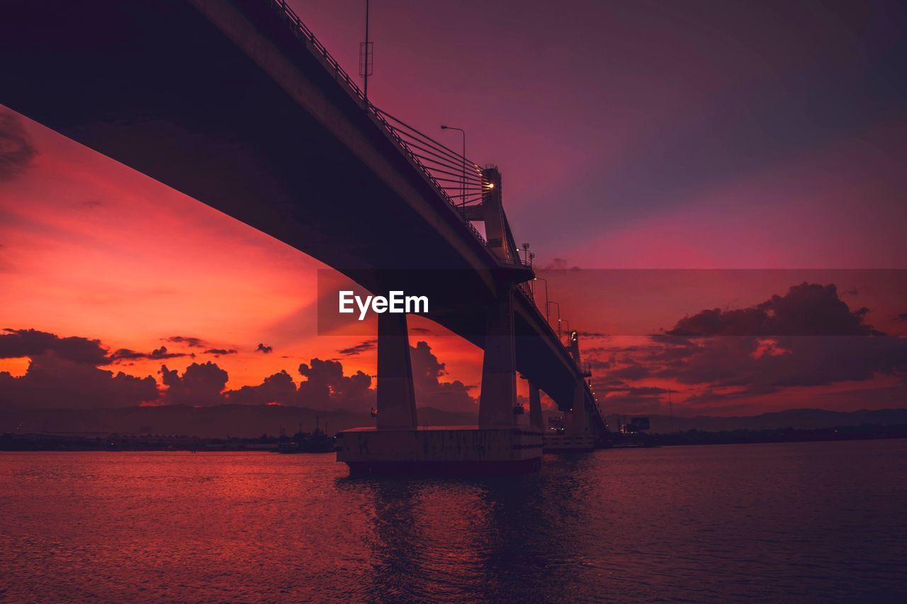 Silhouette bridge over sea against orange sky