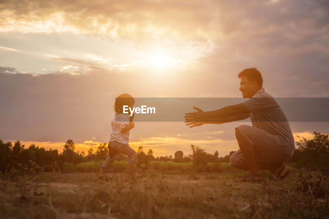 Father with daughter on field against sky during sunset