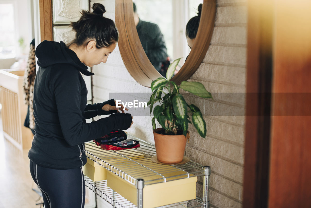 Woman checking diabetes kit while standing in front of mirror at home