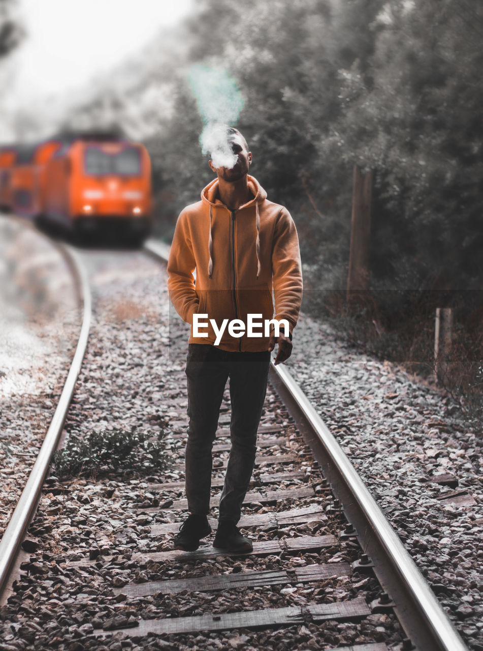 REAR VIEW OF MAN STANDING ON RAILROAD TRACK
