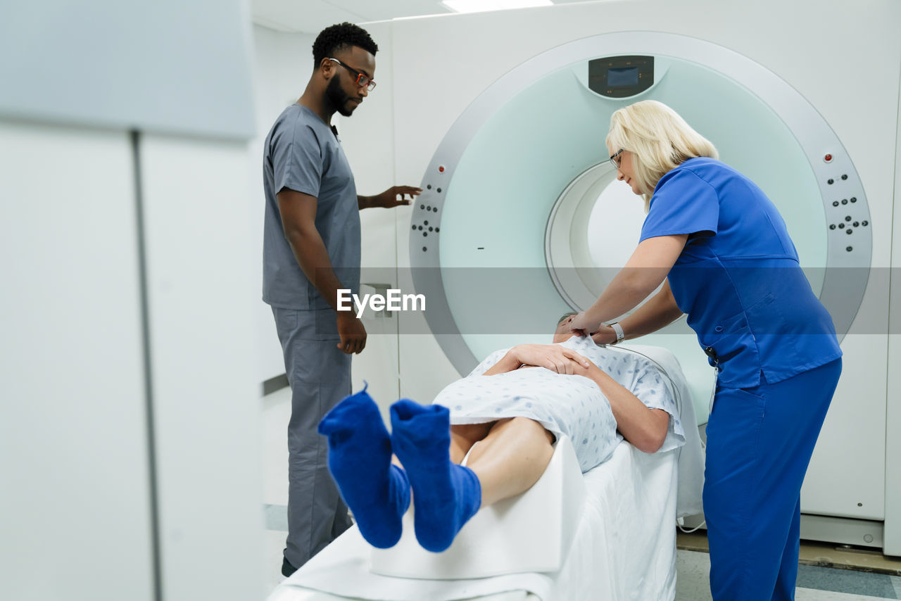 Doctor looking at nurse preparing for mri scan on patient in examination room