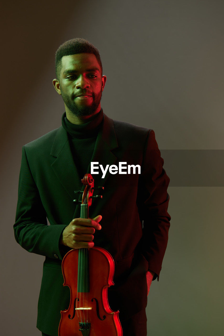 portrait of young man playing violin against black background