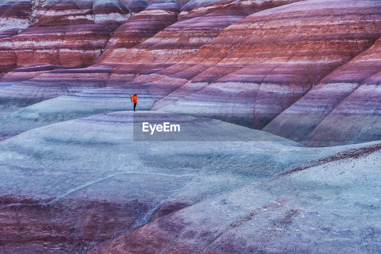 High angle of traveler in outerwear with backpack standing on top of smooth stone formation while exploring bentonite hills in utah, usa