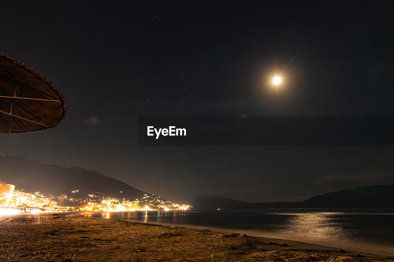 VIEW OF ILLUMINATED BEACH AGAINST SKY AT NIGHT