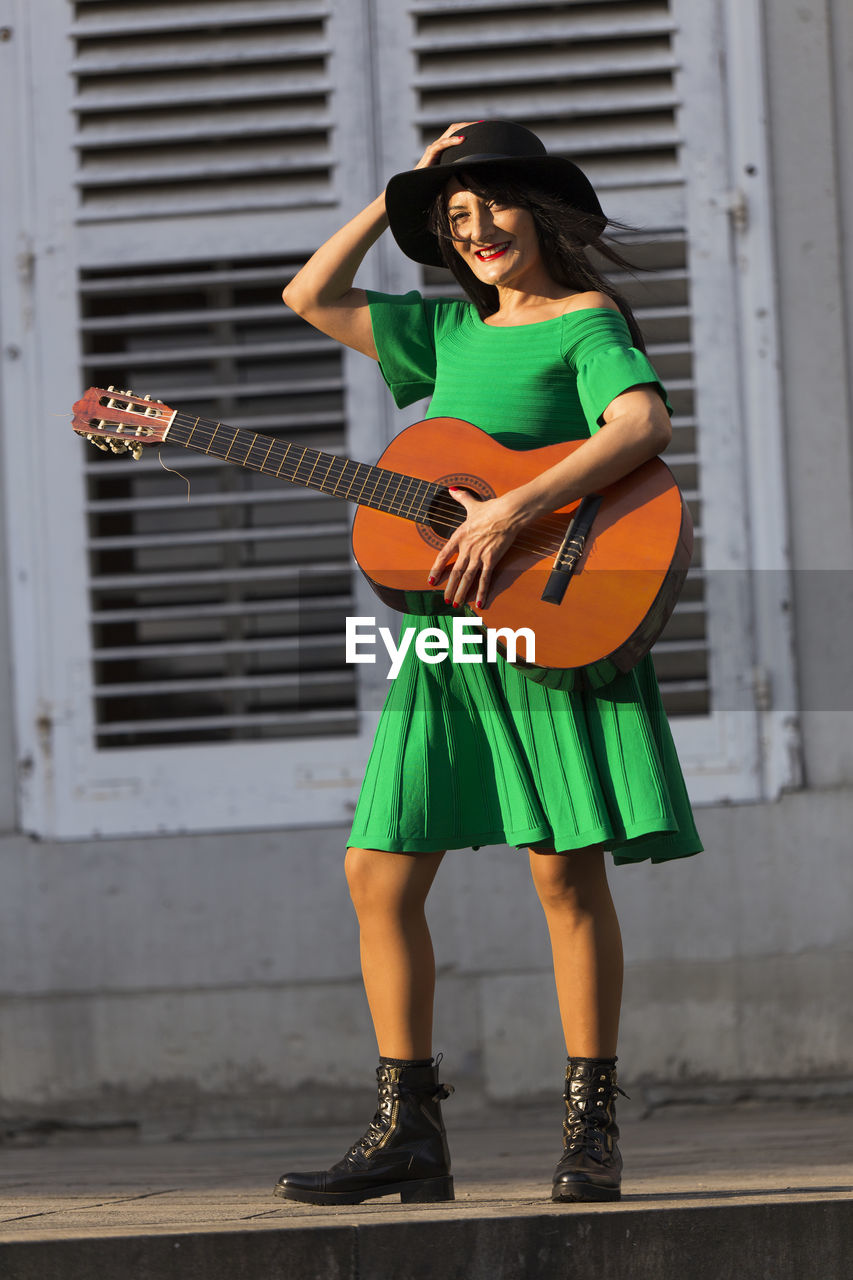 Portrait of woman with guitar walking on footpath